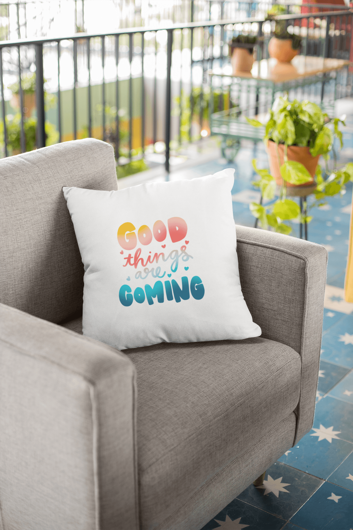 White pillow with colorful "GOOD things are COMING" text resting on a grey fabric armchair.