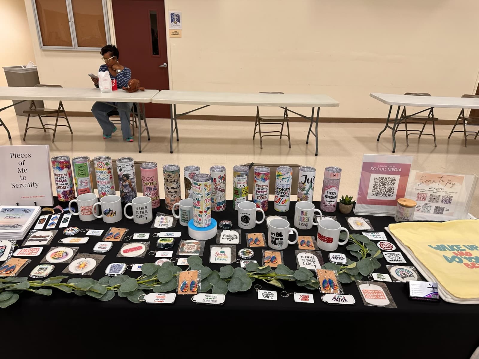 Mental health-themed merchandise including colorful tumblers, mugs, and keychains displayed on a black table.